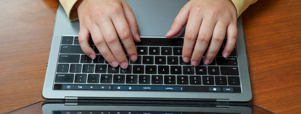 A student's hands type on a laptop keyboard.