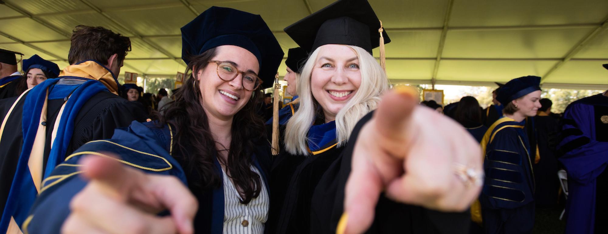 Student and professor pointing and smiling during the MFA and Doctoral Degree Ceremony at University Credit Union Center