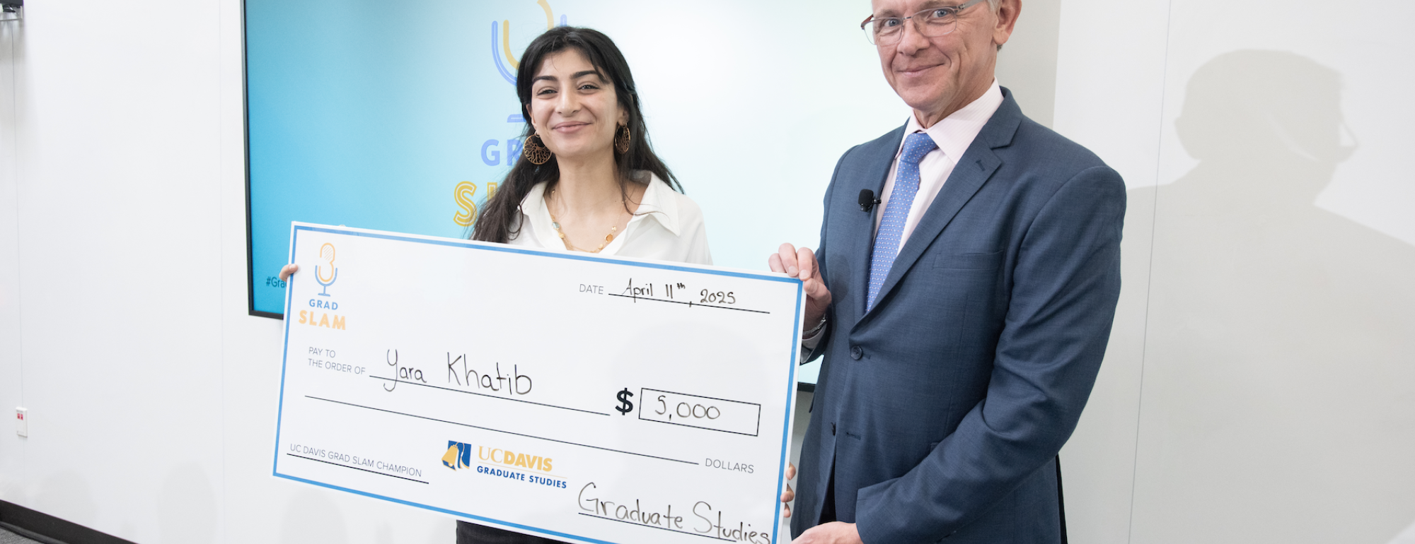 Yara Khatib smiling with giant check next to Dean Jean-Pierre Deplanque.