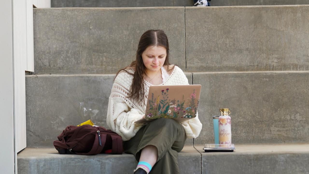Students sitting on stairs looking at computers.