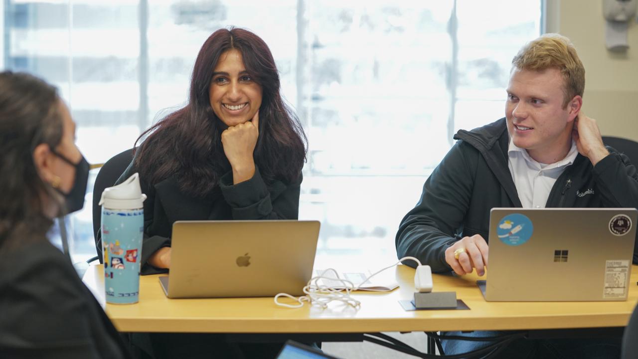 Graduate students smiling with laptops.