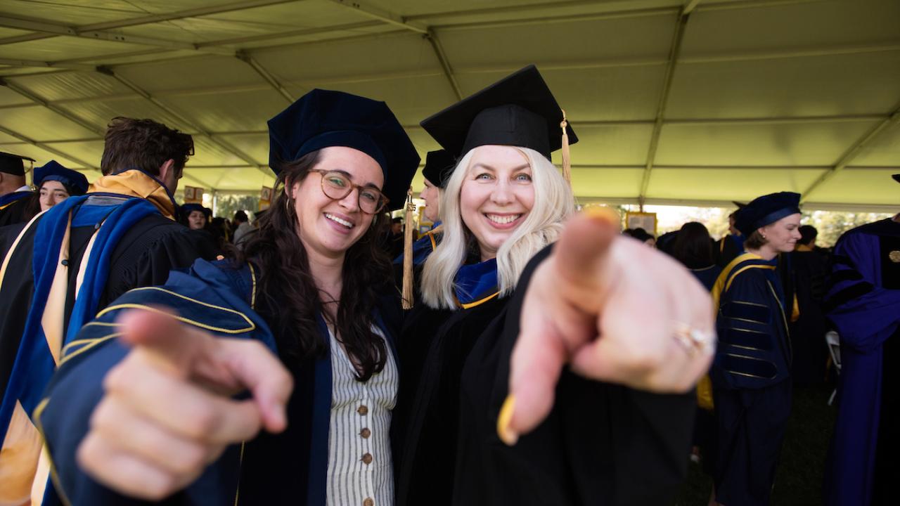 Student and professor pointing and smiling during the MFA and Doctoral Degree Ceremony at University Credit Union Center