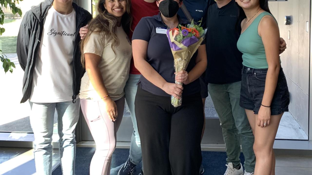 Alyssa Parsons stands in the Conference Center lobby holding a bouquet of flowers surrounded by smiling students