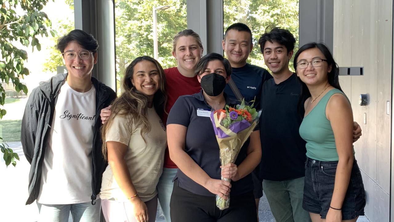 Alyssa Parsons stands in the Conference Center lobby holding a bouquet of flowers surrounded by smiling students