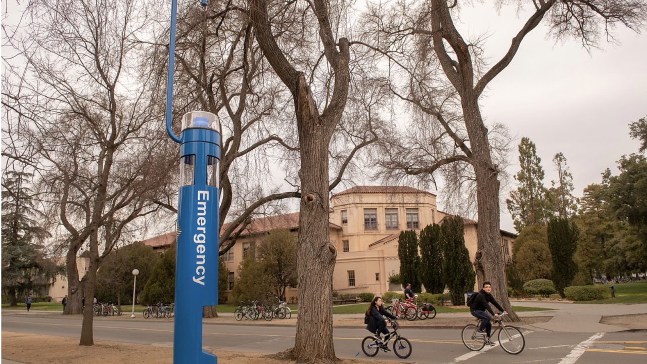 UC Davis students bike past a blue emergency pole located near the bike circle adjacent to Hart Hall.