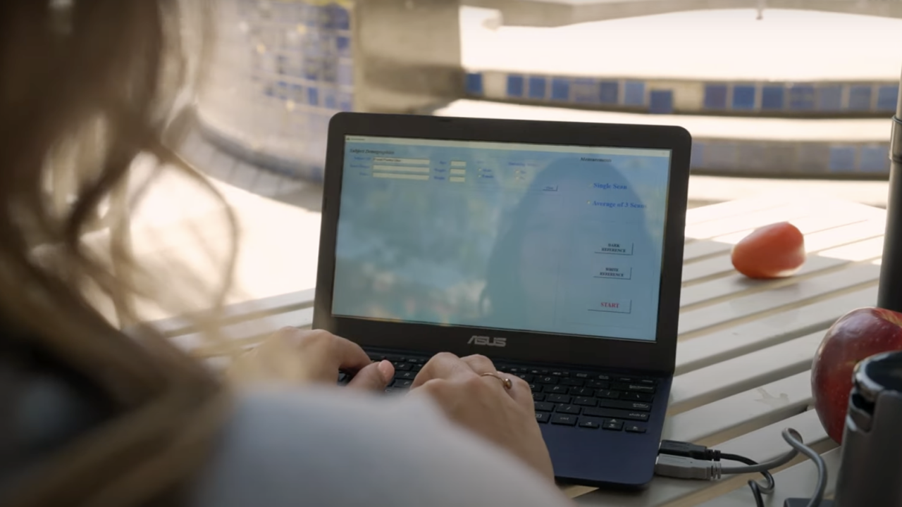 Student works on a small laptop measuring data while sitting at a white picnic table with an apple on the table