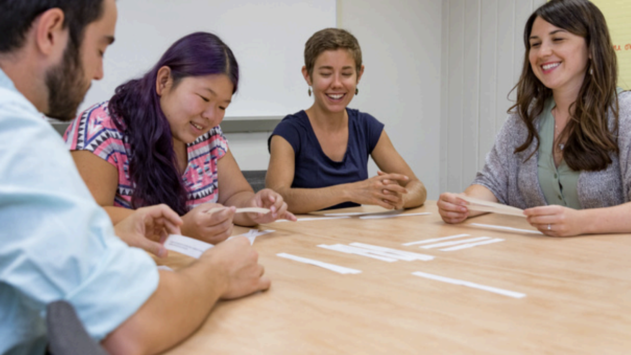 Weekly discussion and reading group smiling and pointing to papers at a desk.