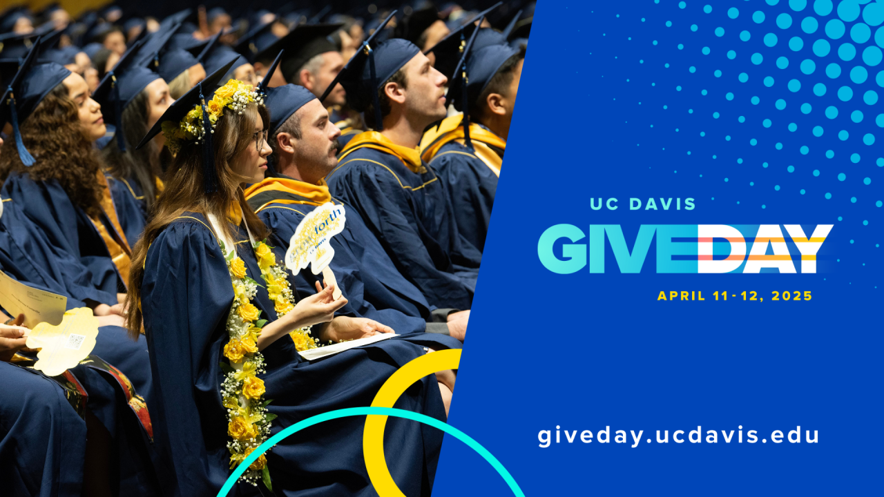 Graduate student at commencement holding "Grow Forth" fan with Give Day logo.