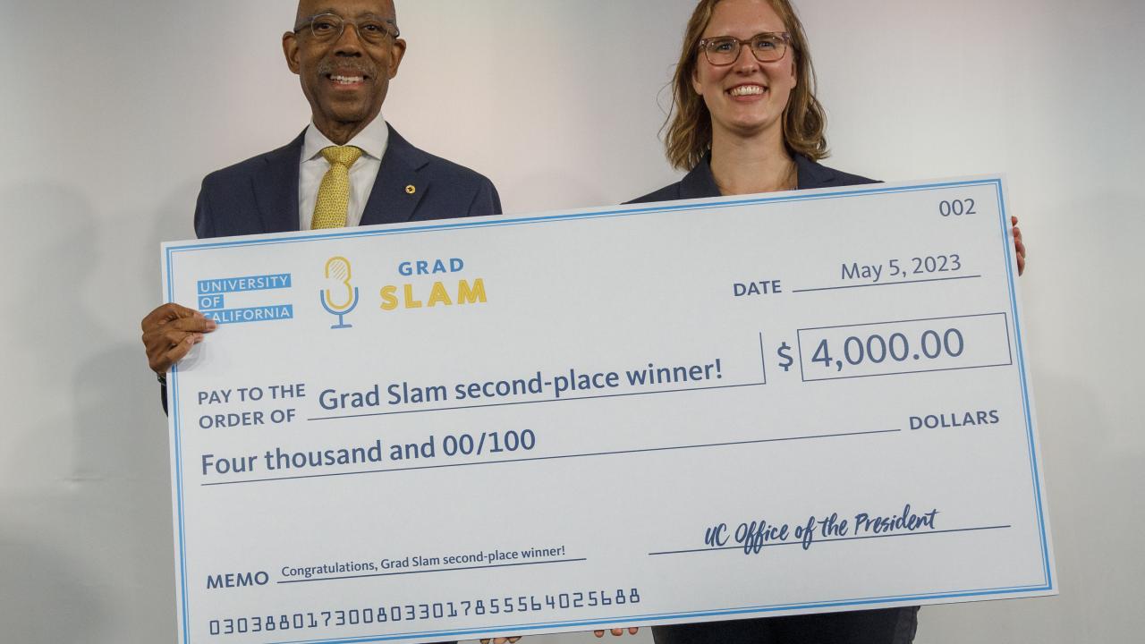 Julia Mouat and UC President Michael Drake pose with an oversized check at the UC Grad Slam Event
