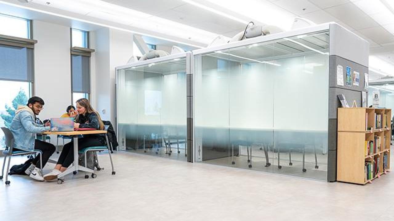 A view of the main Writing Center floor with two students working at a table to the far left.
