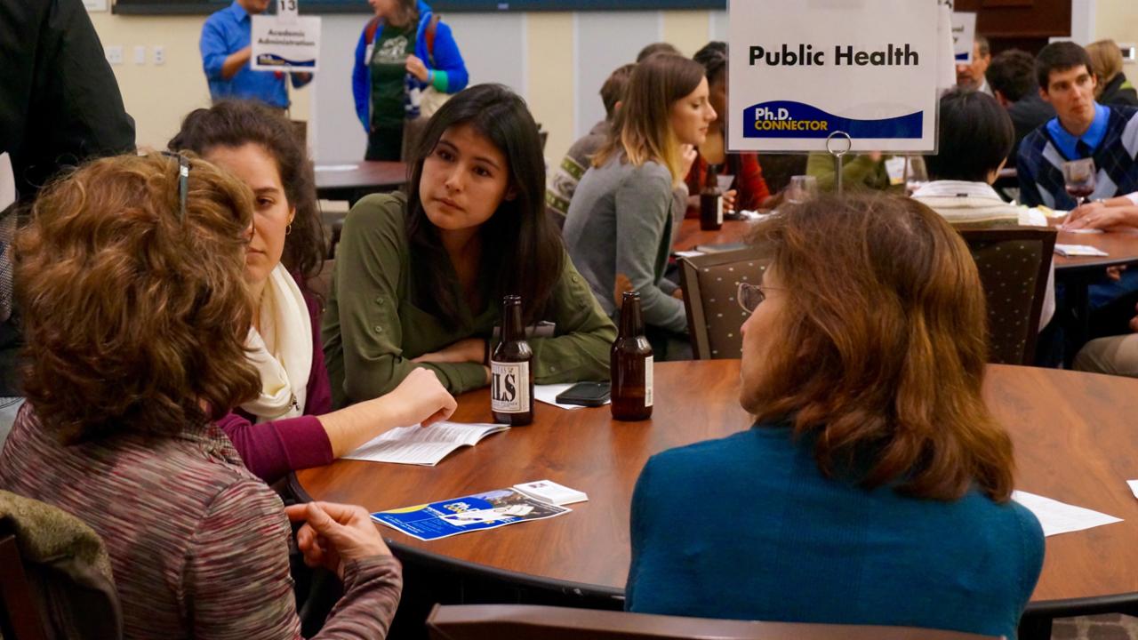 Graduate students and postdocs talk with a career specialist at the Public Health table.