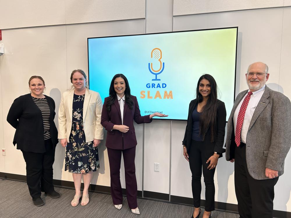 Five judges, (L to R) Dr. Stacey Muse, Dr. Beth Tweedy, Lora Painter, Rinki Sethi, and Dr. Jeff Giebling, pose in front of the UC Davis Grad Slam presentation screen