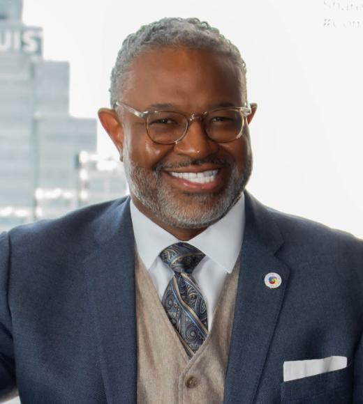 Professional headshot of smiling Dr. Curtis Byrd in navy suit and glasses by office window.