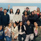 A diverse group of young people posing together, smiling and making playful gestures.