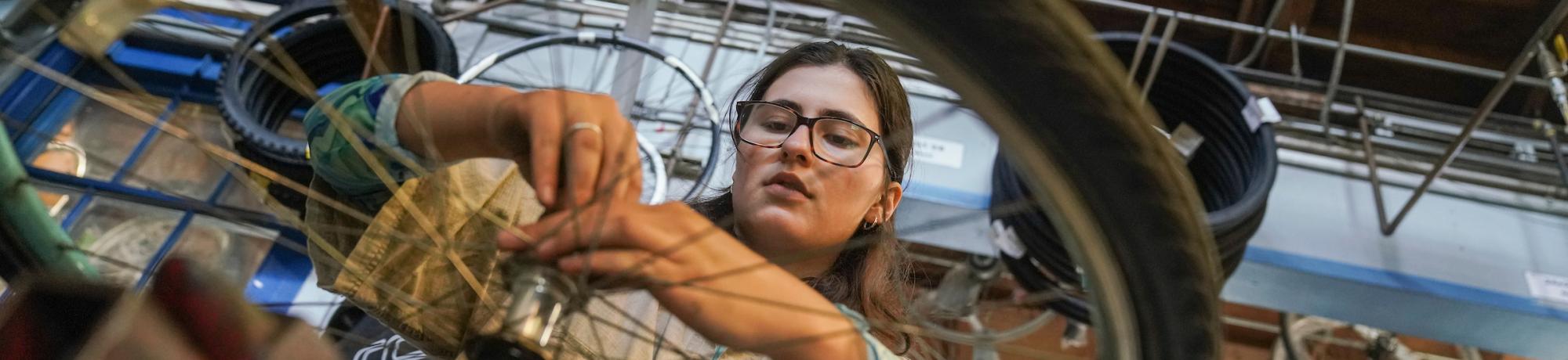 Student wearing glasses uses a tool to fix a bike wheel in the Bike Barn